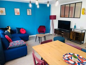 A modern living room with a blue sofa, a wooden dining table, and a TV. - Beautiful 3-bedroom apartment / Porte de Versailles (Paris)