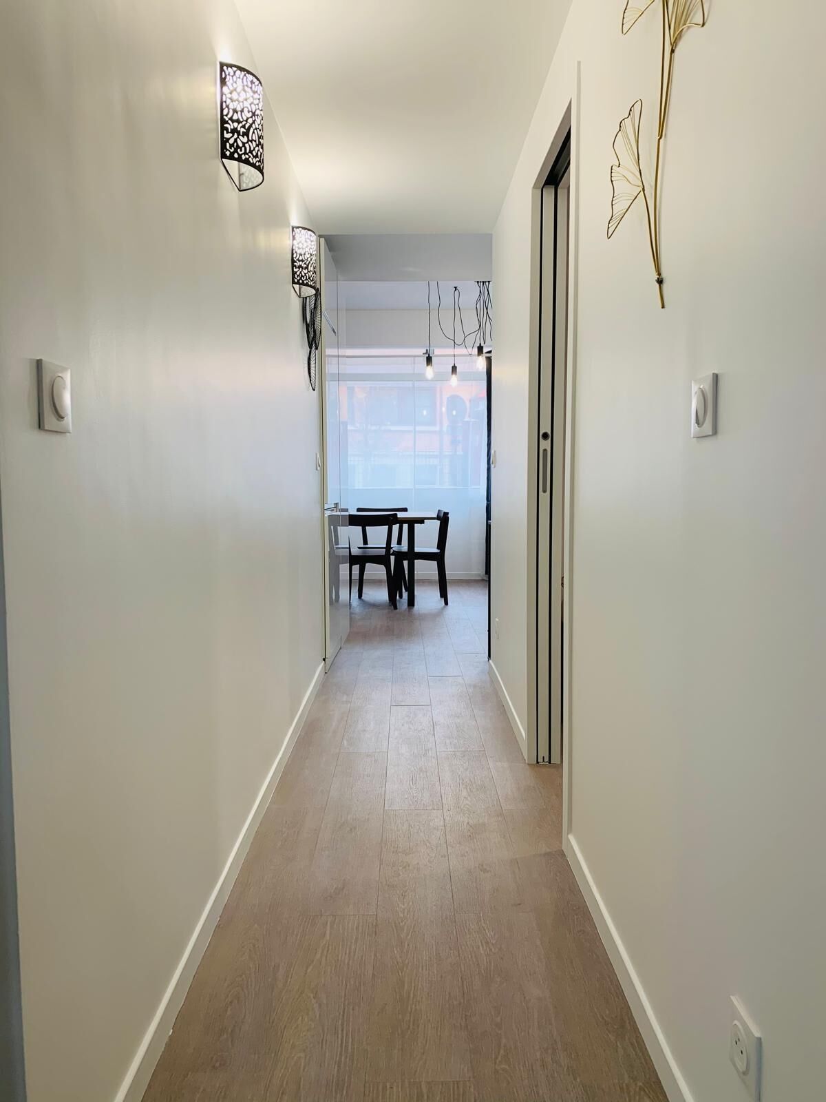 A hallway with a dining area at the end, featuring a table and chairs.