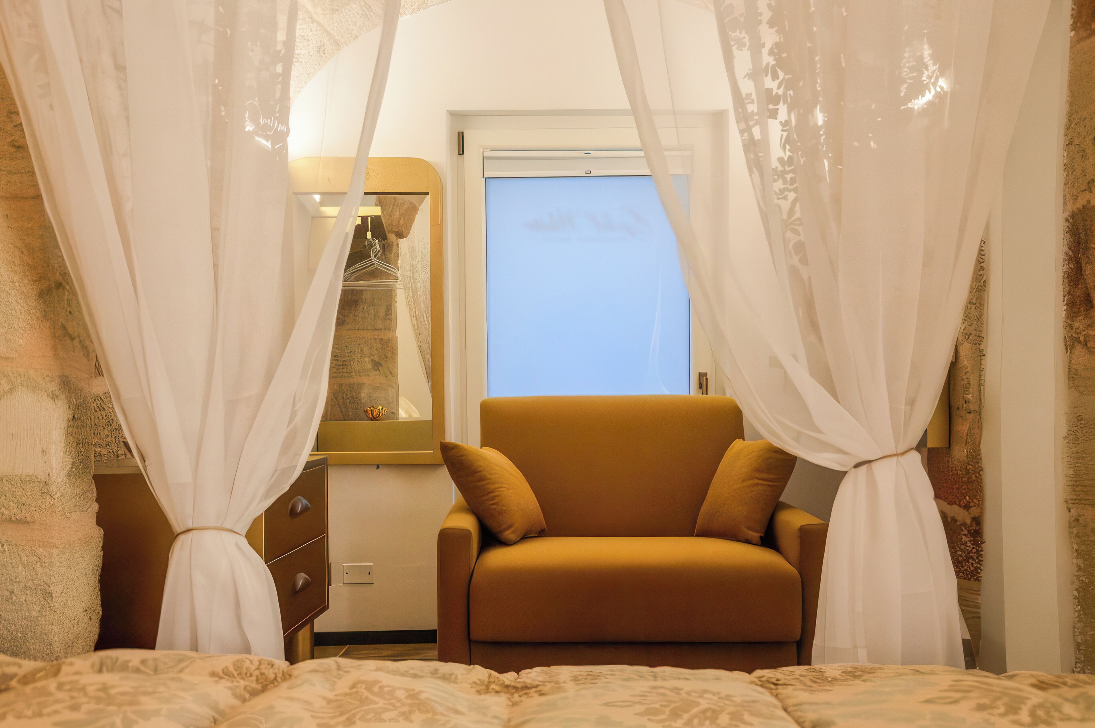 A bedroom with a bed, a sofa, a wardrobe, and a window with curtains.