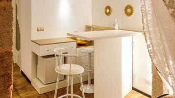 Cocina compacta con encimera blanca, dos taburetes y un refrigerador pequeño.