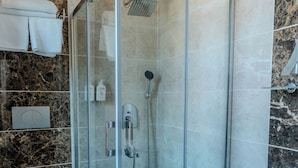 Un baño moderno con ducha envuelta en vidrio, suelo de mármol, inodoro y lavamanos.