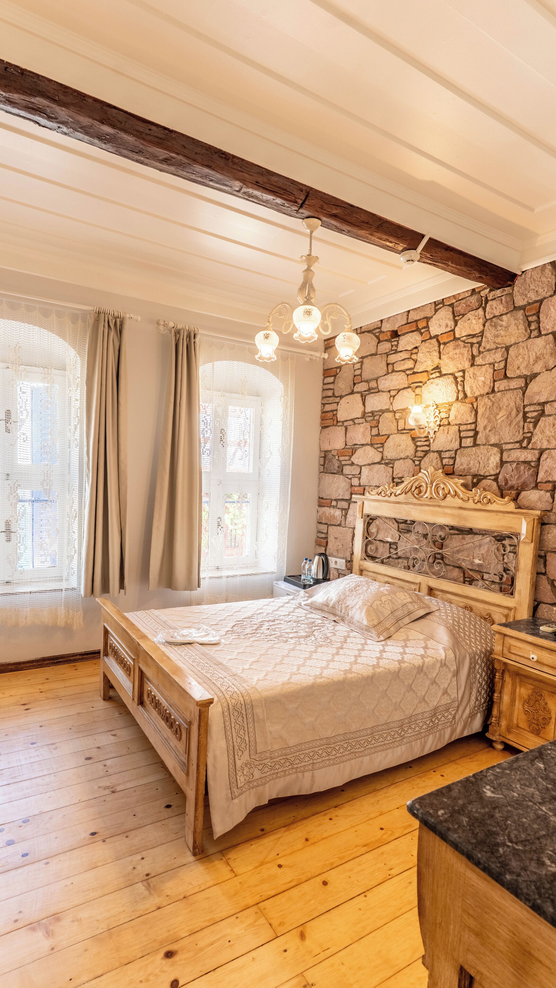 A bedroom with a stone wall, wooden bed frame, and a chandelier.