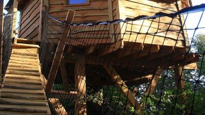 A treehouse with a wooden exterior, a small window, and a wooden staircase leading up to it.