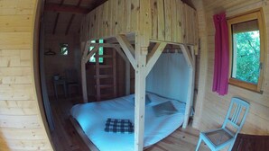 A wooden cabin room with a bed, a chair, and a window.