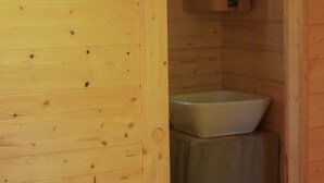 A wooden cabin interior with a wooden wall, a white sink, and a wooden cabinet with a green handle.