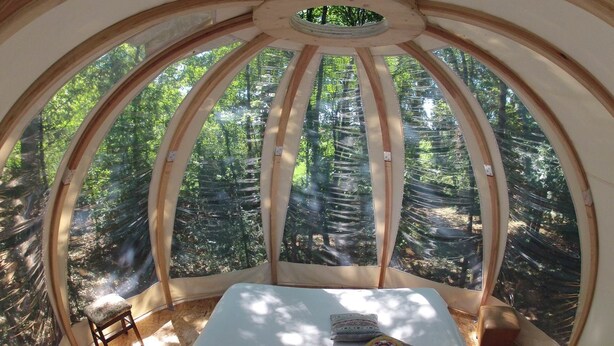 A dome-shaped room with a table, two chairs, and a view of a forest through large windows.