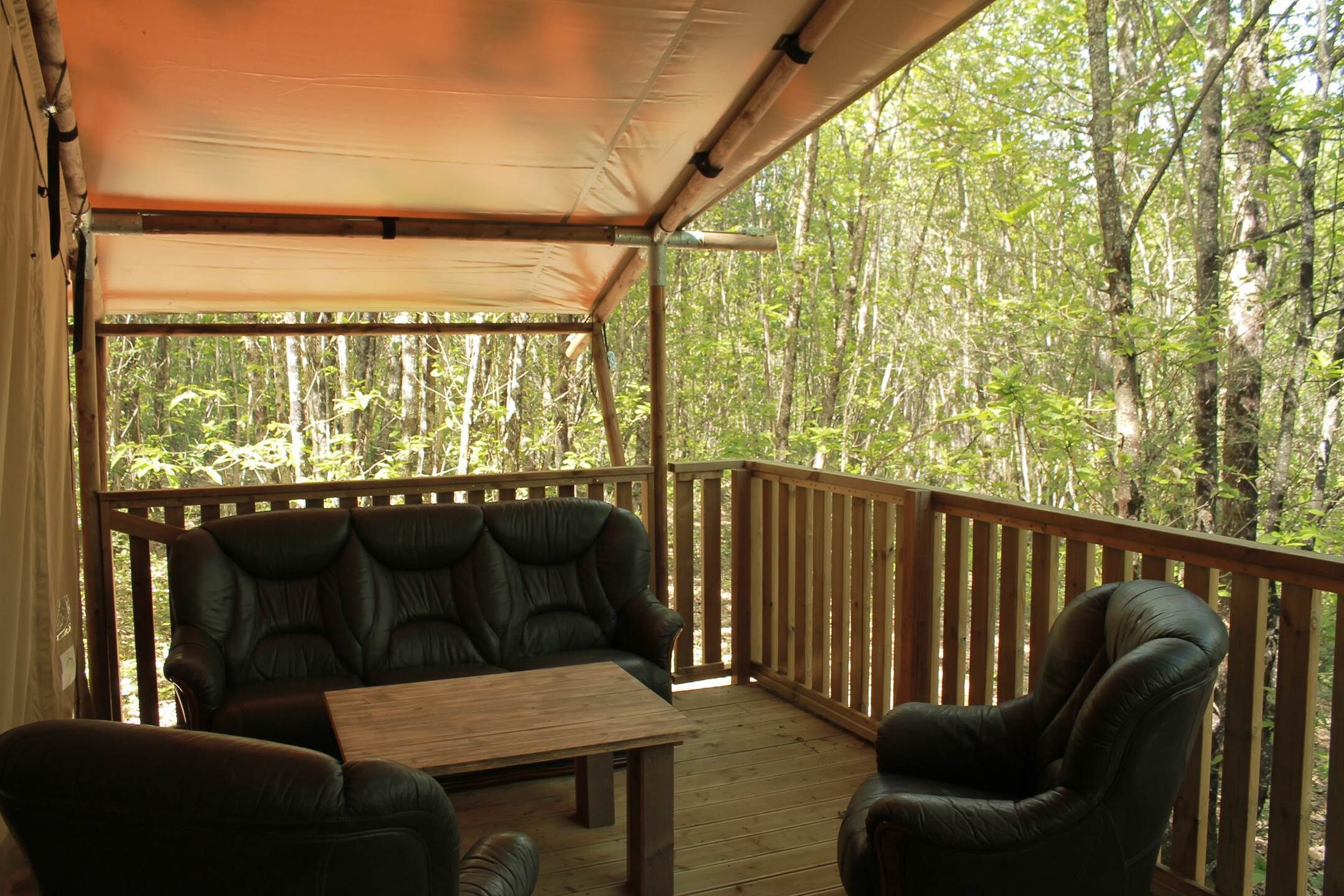 An outdoor deck with a covered seating area, a table, and a view of a forested area.