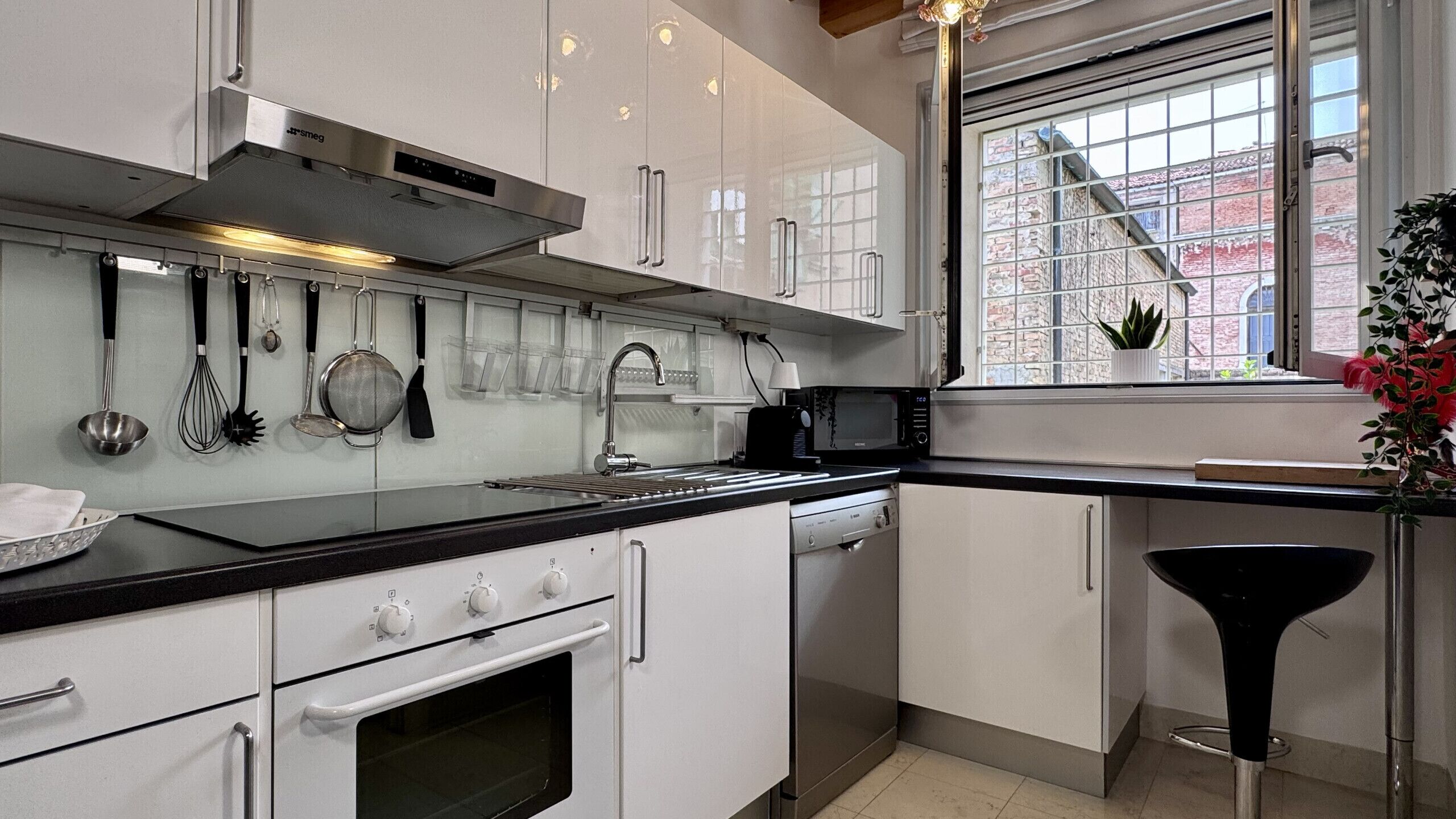 A modern kitchen with white cabinets, stainless steel appliances, and a window with a view of a brick building.