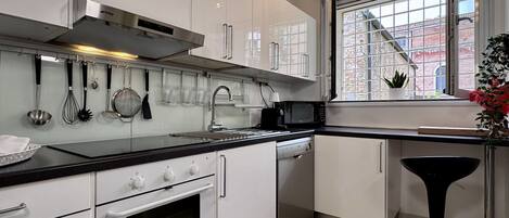 A modern kitchen with white cabinets, stainless steel appliances, and a window with a view of a brick building.