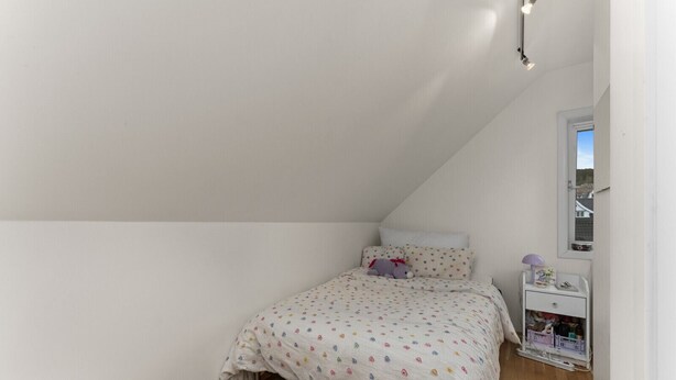 Ein kleines Zimmer mit einem Einzelbett, schrägen Wänden, einem Nachttisch mit Lampe und einem Fenster.