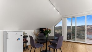 Eine moderne Küche mit einem weißen Kühlschrank, einem runden Tisch mit violetten Stühlen und Blick auf eine Stadt durch große Fenster.