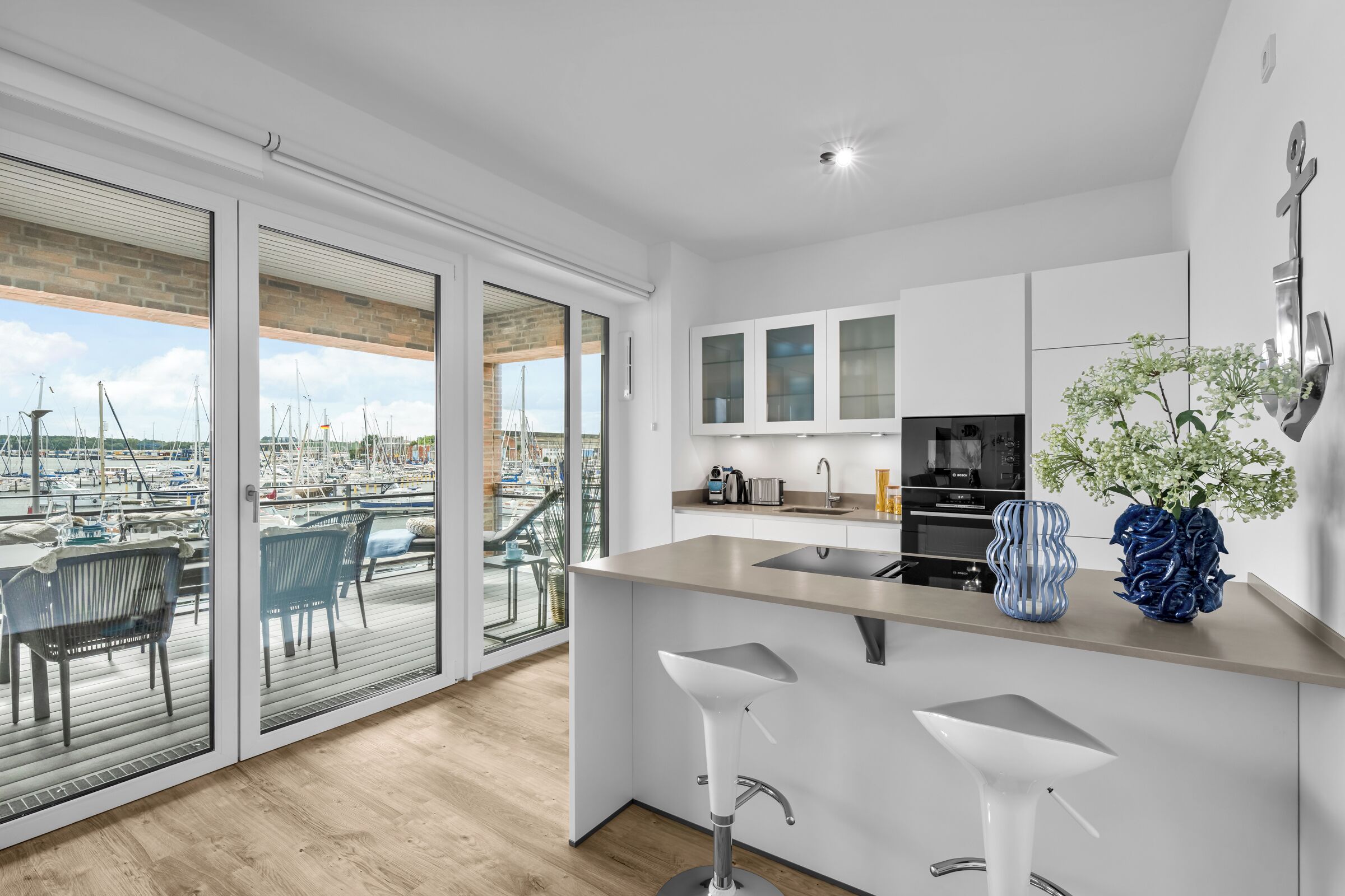 A modern kitchen with a large island, a dining area with a view of a marina, and a balcony with a view of the city.