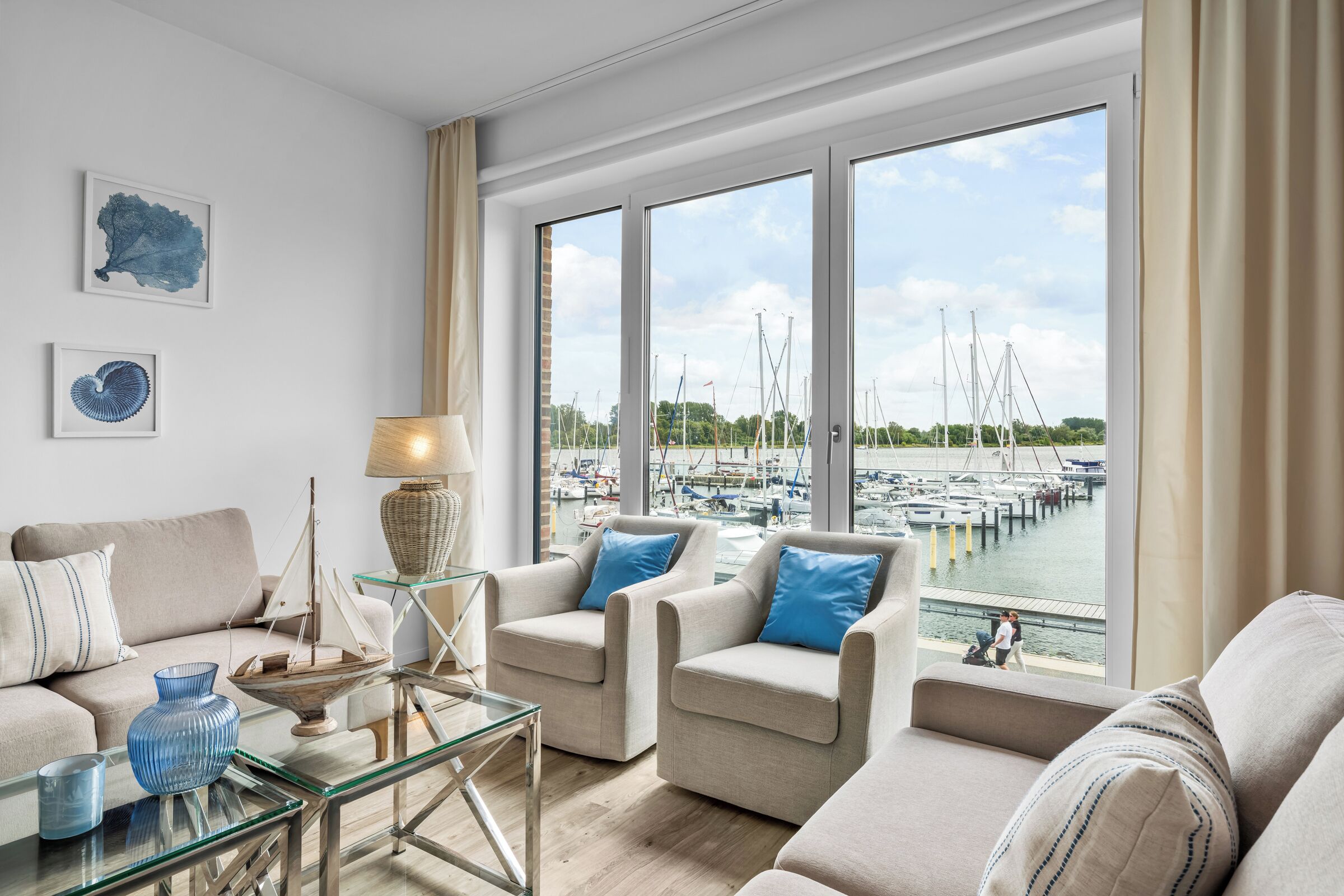 A modern living room with a view of a marina, featuring a sofa set, a glass coffee table, and decorative items.
