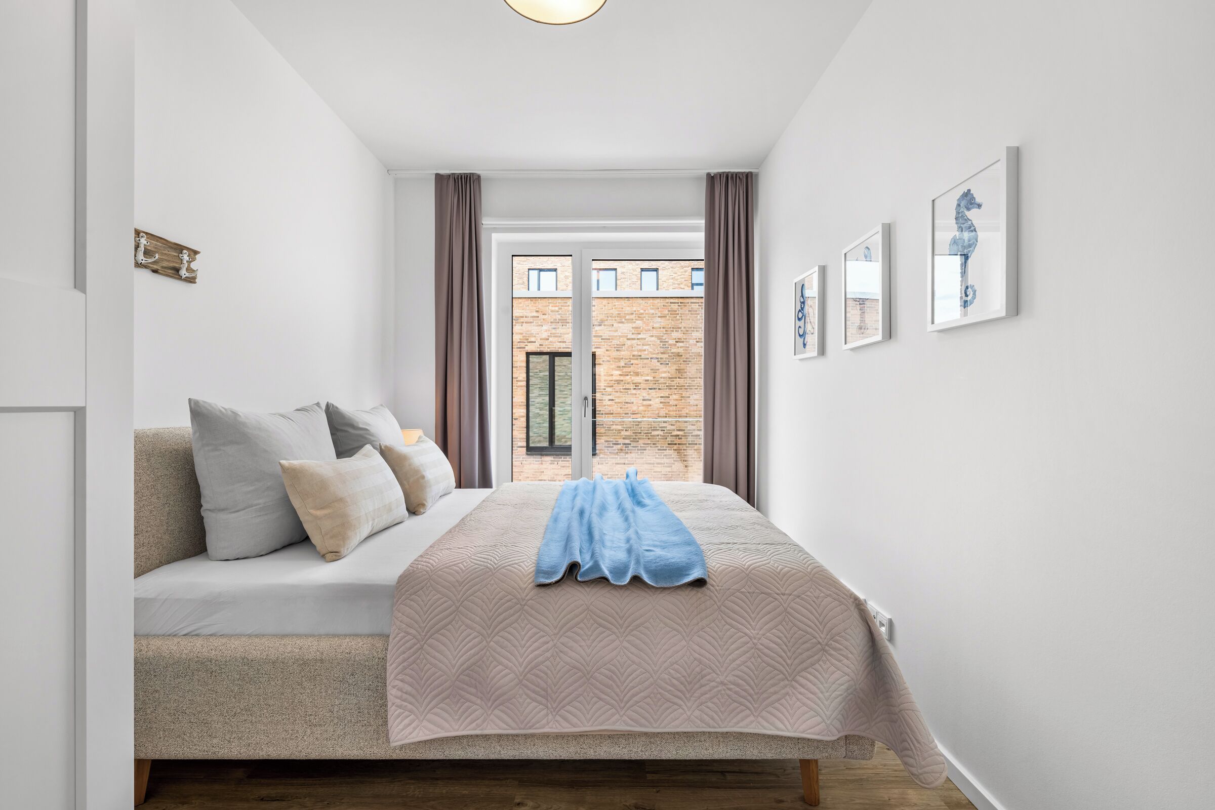A bedroom with a bed, pillows, a blanket, a window with curtains, and a view of a brick building.