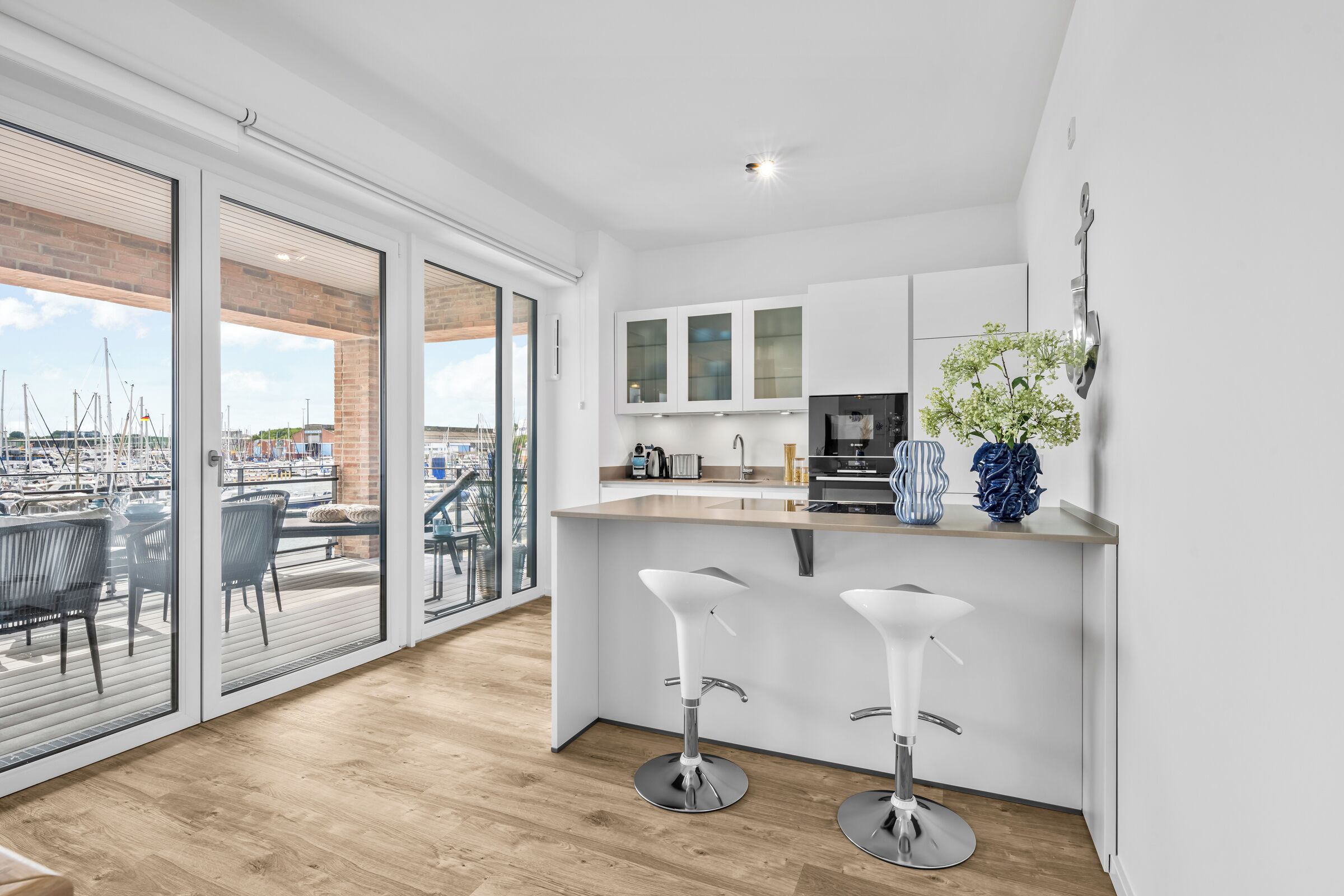 Eine moderne K üche mit einem großen Fenster, einer Essecke mit zwei Barhocker und Blick auf eine Marina.