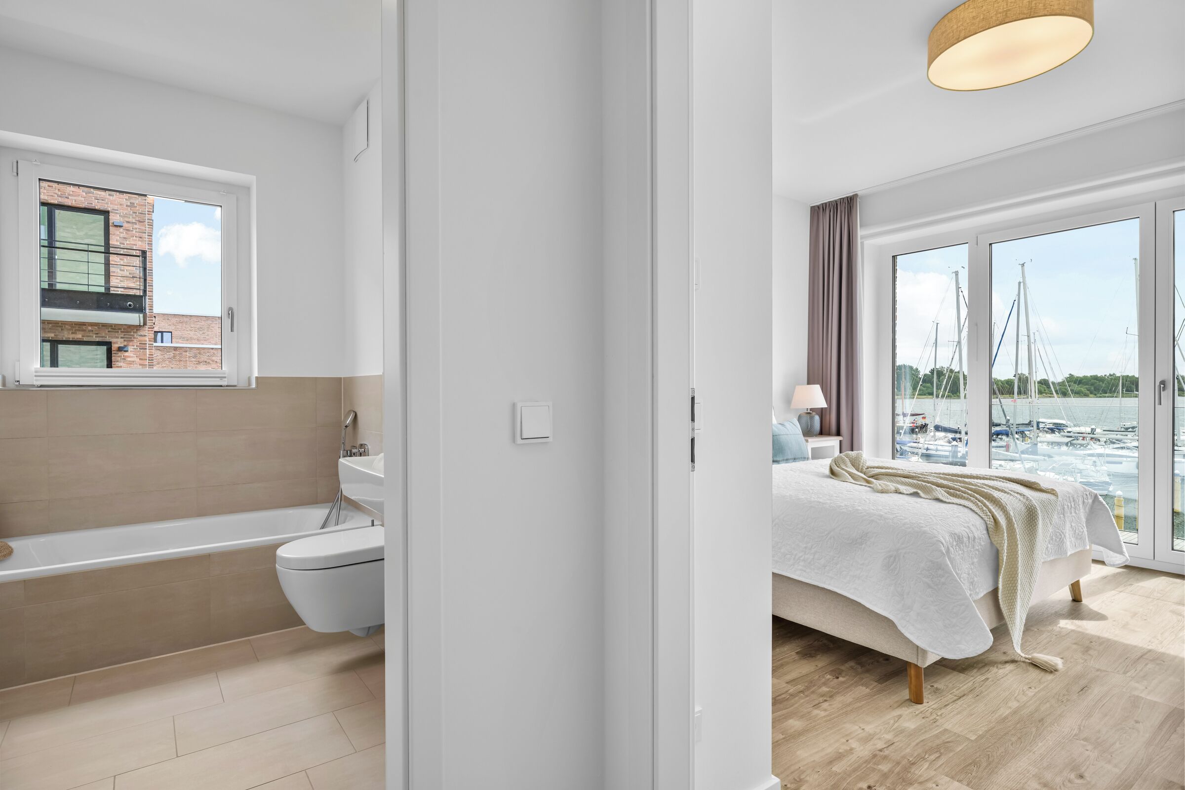 A modern bathroom with a bathtub, toilet, and a window overlooking a marina.