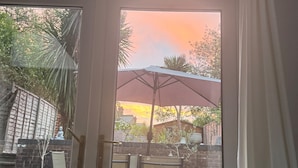 Een terras met buitenmeubilair, een bakstenen muur en uitzicht op de ondergaande zon.