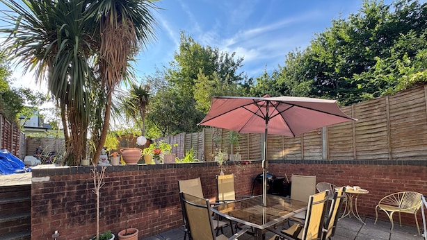 An outdoor patio with a glass table, chairs, and a large umbrella. - Garden Flat - Sleeps 6 (London)