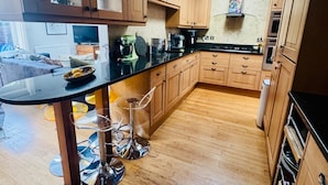Een moderne keuken met houten kastjes, een zwart aanrecht en een glazen kookeiland met barstoelen.
