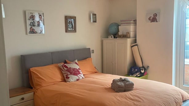 Een slaapkamer met een bed, nachtkastje, kapstok en plafondventilator, en een raam.