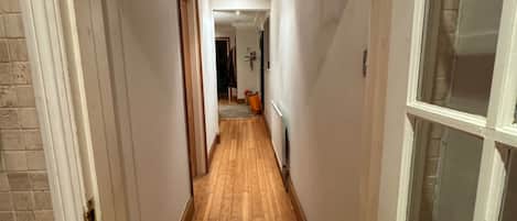A hallway with wooden flooring, white walls, and a door on the right.