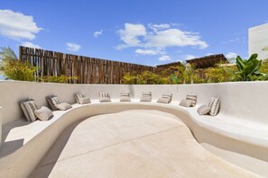 A curved outdoor seating area with cushions, a wooden fence, and tropical plants. - Ka'anal: 2BR Space w 2 Bikes & FREE Beach Shuttle (Tulum Municipality)
