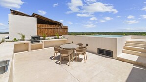 Eine Dachterrasse mit rundem Tisch und Stühlen, einem Grill und einem Swimmingpool im Hintergrund.