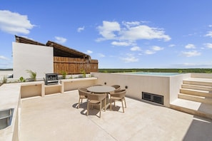 A rooftop patio with a round table and chairs, a barbecue grill, and a swimming pool in the background. - Ka'anal: 2BR Space w 2 Bikes & FREE Beach Shuttle (Tulum Municipality)