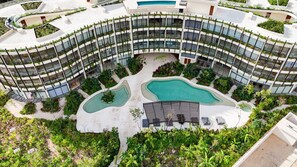 Ein modernes Hotel mit gebogener Architektur, mehreren Balkonen mit Bepflanzung und zwei Schwimmbecken.