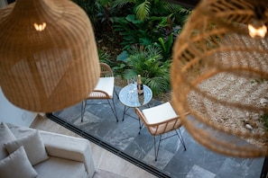 Uma área externa com assentos de vime, mesa de vidro, uma garrafa de champanhe e vista para um jardim com diversas plantas.