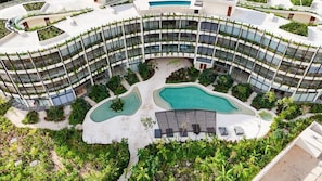 Um hotel com vários andares, fachada curva, diversas varandas e um pátio central com piscina.