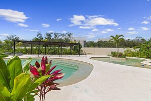 Área de piscina com espaço de estar coberto e céu claro.