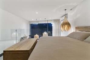 A modern bedroom with a large bed, a wooden nightstand, and a large window with a view of the outdoors. - Stunning Loft in Beautiful Building (Tulum)
