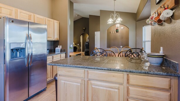 A kitchen with a stainless steel refrigerator, wooden cabinets, granite countertops, and a dining area with chairs and a table. - Single level 3 bedroom house in Pagosa Springs with a fenced backyard (Pagosa Springs)