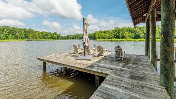 A wooden dock extending into a lake with chairs and an umbrella, surrounded by lush greenery. - The Sanctuary at Morris Creek | 4BR Luxury Stay (Charles City)