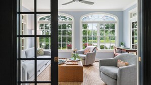 A room with a large arched window, a ceiling fan, a sofa, a chair, and a small table with a plant. - The Sanctuary at Morris Creek | 4BR Luxury Stay (Charles City)