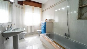 Un baño con lavamanos, inodoro, bañera y una ventana con cortinas.