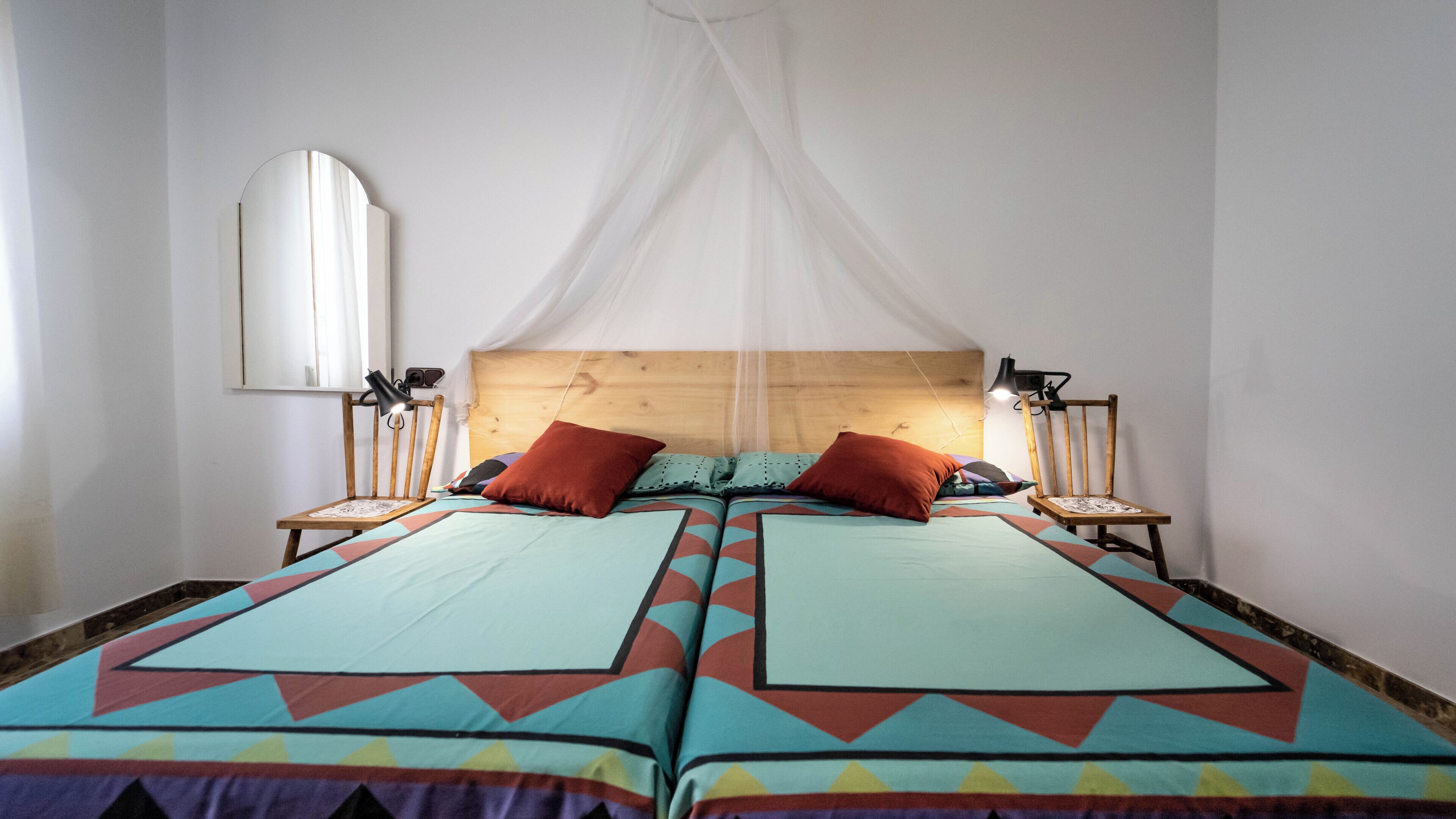 A double bed with a canopy, two bedside lamps, and a mirror on the wall.