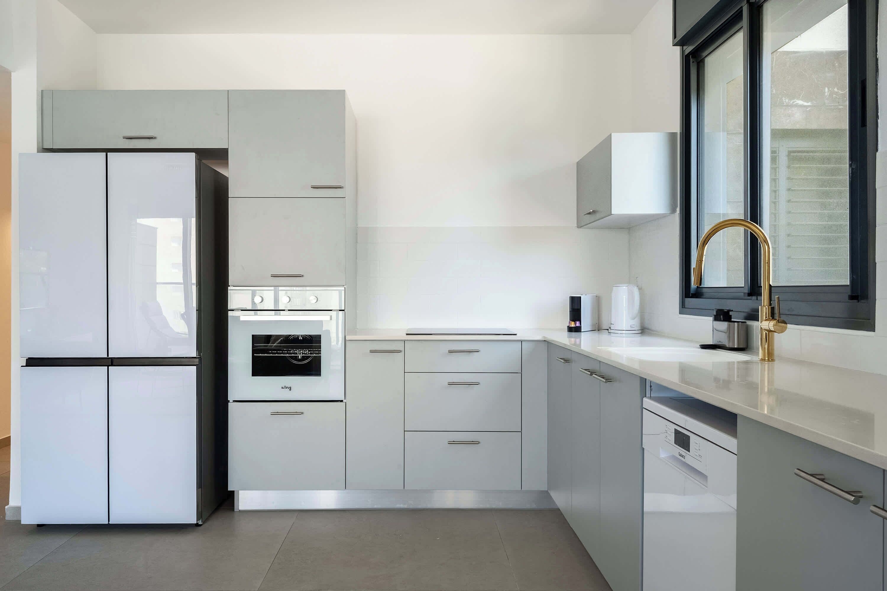 L-shaped kitchen with large refrigerator, white drawers, integrated stove, and substantial storage architecture.
