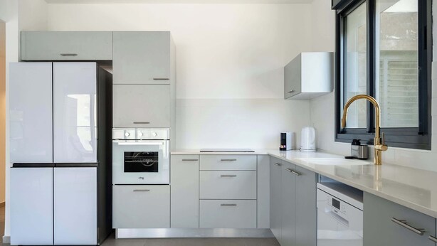 Una cucina moderna con mobili bianchi, forno integrato, lavastoviglie e una finestra con cornice nera.