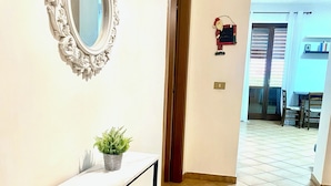 Een gang met een witte marmeren console tafel, een decoratieve spiegel en een potplant.