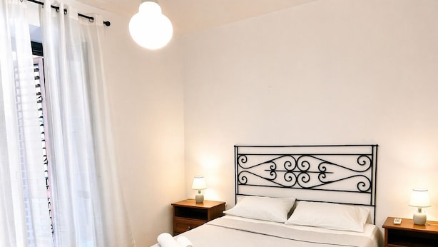 Een slaapkamer met een bed, twee nachtkastjes met lampen, een wit gordijn en een plafondlamp.