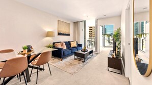 A modern living room with a glass dining table, blue sofa, and a coffee table. - Newstead Balcony Hideaway | Rooftop Pool | Walk to James St & the Valley (Newstead)