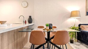A modern kitchen with a glass dining table, four chairs, a clock, and a lamp. - Newstead Balcony Hideaway | Rooftop Pool | Walk to James St & the Valley (Newstead)