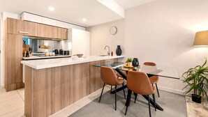 A modern kitchen with a central island, wooden cabinets, and a dining area with chairs. - Newstead Balcony Hideaway | Rooftop Pool | Walk to James St & the Valley (Newstead)