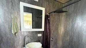 Un baño moderno con lavamanos blanco, espejo, toalla, ducha y retrete.