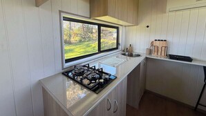 Cocina compacta con estufa a gas, un lavamanos y un ventanal con vistas a un paisaje verde.