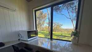 Cocina compacta con microondas, refrigerador pequeño y ventana que ofrece vistas a un área verde y árboles.
