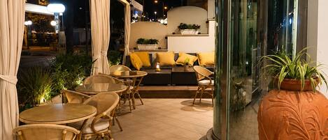 A modern interior with a round dining table, wicker chairs, a sofa with yellow cushions, and a large decorative pot.