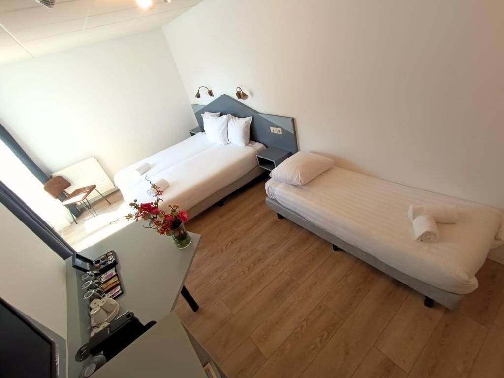 A hotel room with two single beds, a small desk with a chair, and a window.